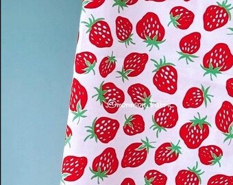 May include: White fabric with a repeating pattern of red strawberries with green stems and leaves. The strawberries are of varying sizes and are scattered across the fabric. The background is white.