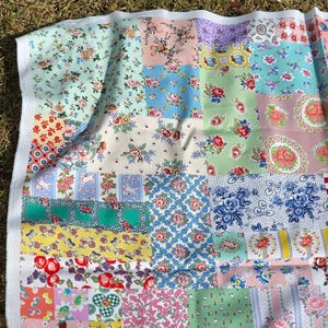 May include: A patchwork quilt with a variety of floral patterns in shades of pink, blue, green, and yellow. The quilt is made of squares of fabric sewn together, creating a colorful and textured design. The quilt has a white border.