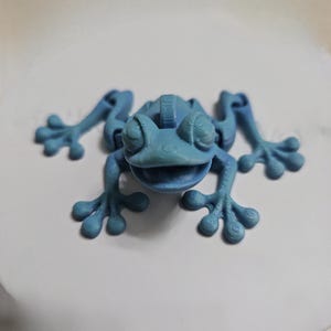 May include: A blue 3D printed frog figurine with a textured surface and a wide open mouth. The frog has four legs and four toes on each foot.