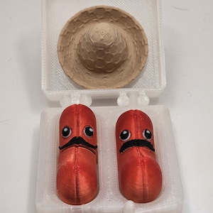 May include: A 3D-printed novelty set featuring a miniature sombrero and two red, cartoon-like figures with black mustaches and googly eyes, all housed in a clear plastic container.
