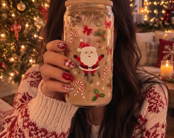 May include: A clear glass tumbler with a bamboo lid and a glass straw, filled with a light brown beverage. The exterior features a festive print of Santa Claus, red bows, candy canes, and green holly leaves with small white snowflakes.