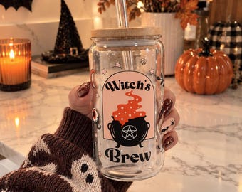 May include: A clear glass tumbler with a bamboo lid and a glass straw. The front features a graphic of a black cauldron with a pentagram, orange bubbling liquid, and the text Witch's Brew inside a pink arch, surrounded by small stars and moons.