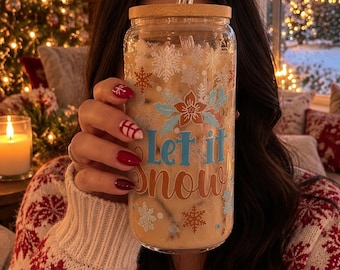 May include: A clear glass tumbler with a bamboo lid and a glass straw, featuring a printed design of blue and orange snowflakes, a poinsettia flower, and the text Let it snow in blue and orange script lettering, filled with a beige beverage.
