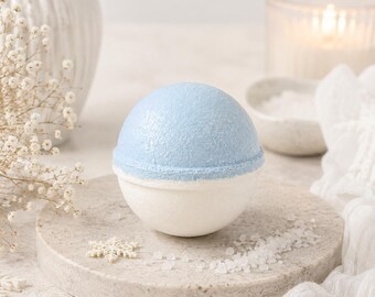 May include: A spherical bath bomb featuring a light blue top half with a textured, glittery finish and a smooth, solid white bottom half. The bath bomb is positioned centrally, showcasing a distinct horizontal seam where the two colored halves meet.