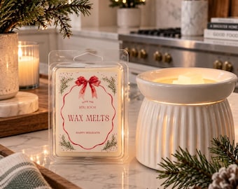 May include: A clear plastic clamshell package of wax melts with a label featuring a red bow, green pine branches, and the text Love the Reiki Room Wax Melts Happy Holidays, positioned next to a white ceramic wax warmer with a ribbed exterior.