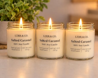 May include: Three clear glass jar candles with lit wicks. Each label reads LTRR & CO. Salted Caramel 100% Soy Candle, Hand poured, Small batch, NET WT. 8 OZ (227 g). The wax is off-white, and the flames emit a warm, glowing light.