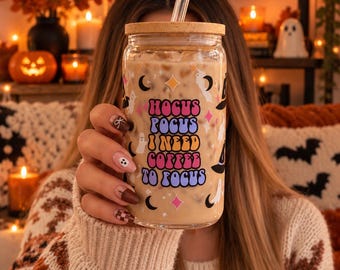 May include: A clear glass tumbler with a bamboo lid and a glass straw, filled with iced coffee. The glass features a colorful graphic print with the text Hocus Pocus I Need Coffee To Focus, surrounded by small illustrations of ghosts, stars, and moons.