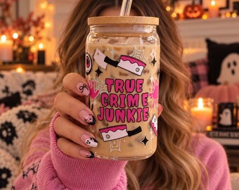 May include: A clear glass tumbler with a bamboo lid and a glass straw, filled with an iced beverage. The exterior features pink text reading TRUE CRIME JUNKIE, surrounded by graphic illustrations of cleavers, eyeballs, and spider webs.