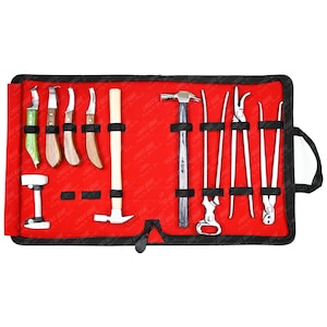 Op de afbeelding: Een rode gereedschapsrol met een zwarte rand, met diverse metalen en houten gereedschappen. De gereedschappen omvatten hamers, messen en tangen. De rol heeft een zwarte handgreep en een zwarte sluiting.