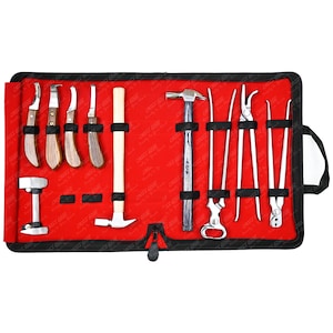 Puede incluir: Un conjunto de herramientas de metalurgia expuestas sobre un rollo de tela roja. Las herramientas incluyen varios cuchillos, martillos y alicates, todos cuidadosamente dispuestos. El rollo tiene un borde negro y un asa. Herramientas para dar forma y reparar metal.