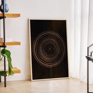 May include: A black and gold mandala print with a geometric design. The print is framed in a white frame and is hanging on a white wall.