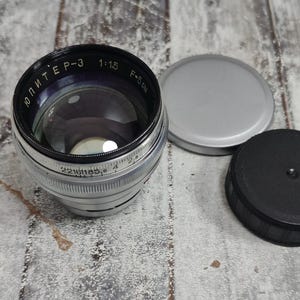 Pu&ograve; includere: Un obiettivo per fotocamera Jupiter-3 vintage con corpo argentato e nero, lente in vetro trasparente e tappo dell'obiettivo nero e argento. L'obiettivo presenta le scritte "Jupiter-3 1:1.5 F=5cm". &Egrave; presente anche un tappo dell'obiettivo argentato.