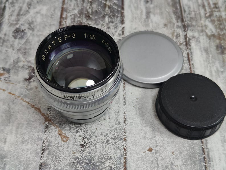 Pu&ograve; includere: Un obiettivo per fotocamera Jupiter-3 vintage con corpo argentato e nero, lente in vetro trasparente e tappo dell'obiettivo nero e argento. L'obiettivo presenta le scritte "Jupiter-3 1:1.5 F=5cm". &Egrave; presente anche un tappo dell'obiettivo argentato.