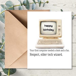 May include: A birthday card with a vintage computer illustration. The screen displays "happy birthday." Below the computer is a keyboard. The card includes the text: "Your first computer needed a desk and a fan. Respect, elder tech wizard."