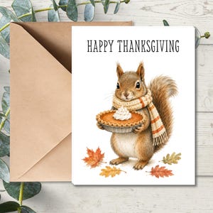 May include: A white greeting card featuring a brown squirrel wearing a cream and orange striped scarf, holding a pumpkin pie with whipped cream. The text HAPPY THANKSGIVING is printed in black above the squirrel, with colorful autumn leaves below.