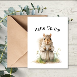 May include: A greeting card with a watercolor illustration of a squirrel holding a cup, wearing a coat, and surrounded by grass and flowers. The words "Hello Spring" are printed at the top. A brown envelope is next to the card.