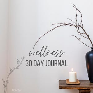 Puede incluir: Una composición minimalista con un jarrón negro con ramas, una vela encendida sobre una bandeja de madera y el texto "wellness 30 DAY JOURNAL" en una pared blanca. La escena evoca calma y bienestar.