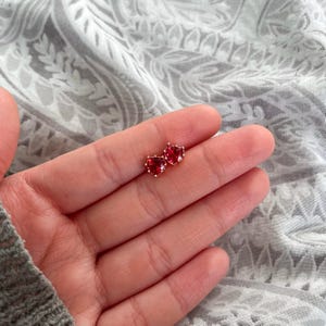 May include: A pair of heart-shaped earrings with red gemstones set in gold.