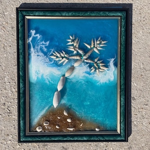 May include: Framed artwork depicting a beach scene. The art features a blue and white ocean, a sandy shore, and a palm tree made of seashells. The frame is dark green with a gold inner border.