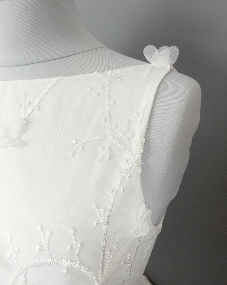 May include: White sleeveless dress with delicate floral embroidery and tulle flower accents on the shoulders.