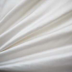 May include: A close-up of a smooth, white fabric with soft folds and wrinkles.
