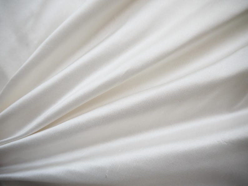 May include: A close-up of a smooth, white fabric with soft folds and wrinkles.