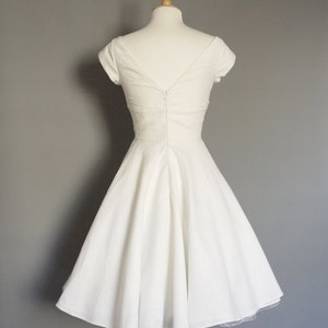 Puede incluir: Un vestido blanco sin mangas, de corte A, con escote en V y cremallera en la espalda. El vestido est&aacute; en un maniqu&iacute; y tiene una falda interior de tul.