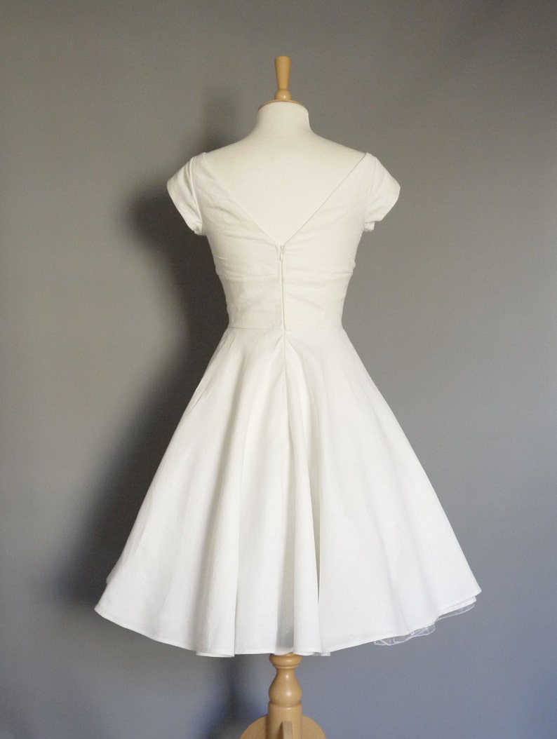 Puede incluir: Un vestido blanco sin mangas, de corte A, con escote en V y cremallera en la espalda. El vestido est&aacute; en un maniqu&iacute; y tiene una falda interior de tul.