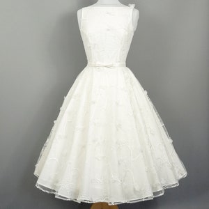 May include: A white sleeveless wedding dress with a full skirt and a delicate floral pattern. The dress has a fitted bodice and a satin sash at the waist.