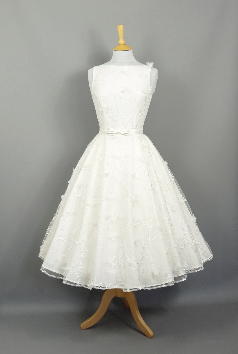 May include: A white sleeveless wedding dress with a full skirt and a delicate floral pattern. The dress has a fitted bodice and a satin sash at the waist.