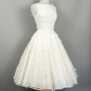 May include: A white sleeveless wedding dress with a full skirt and delicate floral embroidery. The dress has a bateau neckline and is fitted at the bodice.