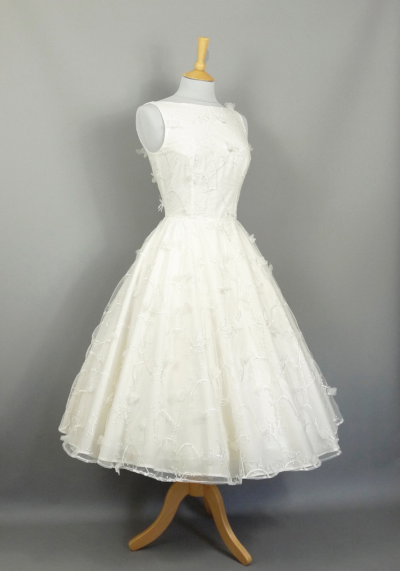 May include: A white sleeveless wedding dress with a full skirt and delicate floral embroidery. The dress has a bateau neckline and is fitted at the bodice.
