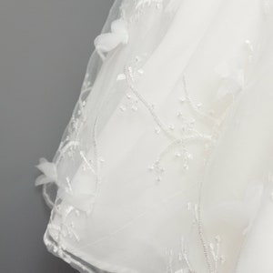 May include: White tulle fabric with delicate floral embroidery. The fabric is sheer and has a soft, flowing texture.