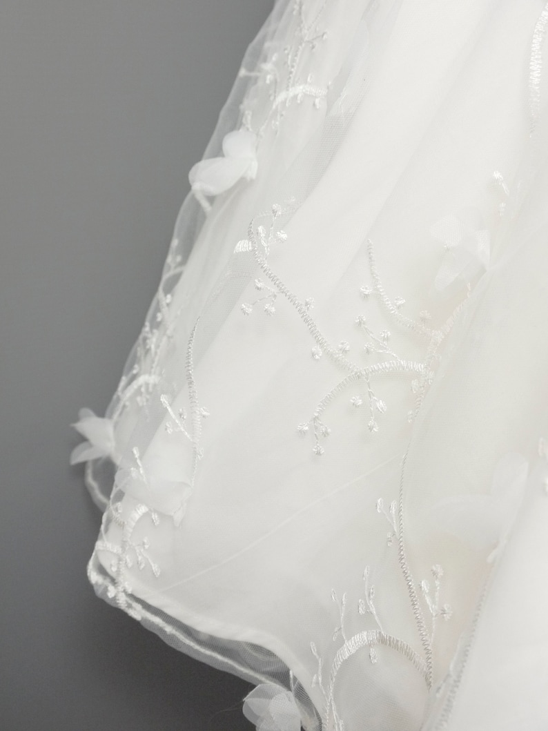 May include: White tulle fabric with delicate floral embroidery. The fabric is sheer and has a soft, flowing texture.