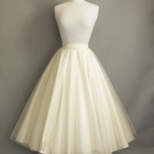 May include: A white tulle skirt with a satin waistband. The skirt is full and flowing, and it is displayed on a mannequin against a gray background.