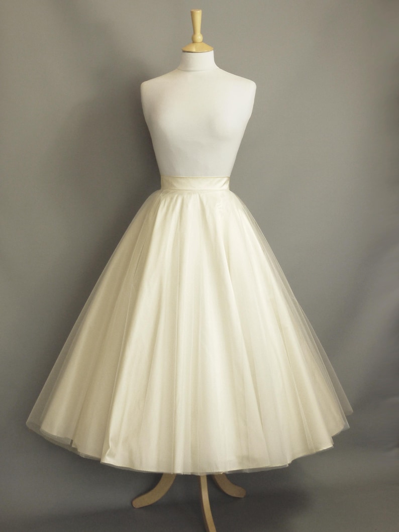 May include: A white tulle skirt with a satin waistband. The skirt is full and flowing, and it is displayed on a mannequin against a gray background.