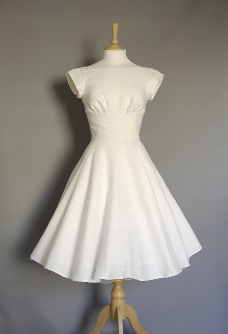 Puede incluir: Un vestido blanco sin mangas, de corte A, con un corpi&ntilde;o ajustado y una falda amplia. El vestido est&aacute; en un maniqu&iacute; de madera.