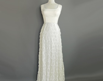 May include: A white sleeveless maxi dress with a fitted bodice and a skirt made of fringe. The fringe is arranged in a pattern of overlapping scales.