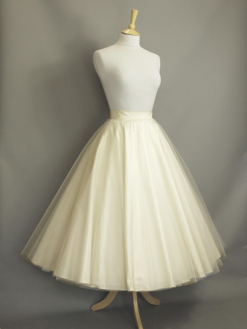 May include: A white tulle skirt with a satin waistband. The skirt is full and flowing, and it is displayed on a mannequin against a gray background.
