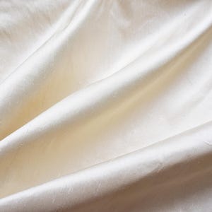 May include: A close-up of a smooth, off-white fabric with soft folds and wrinkles.