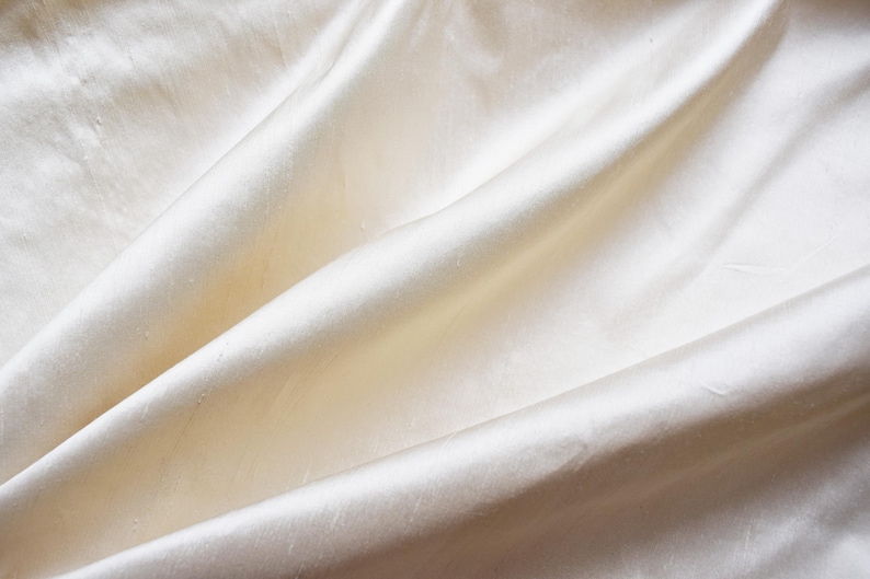 May include: A close-up of a smooth, off-white fabric with soft folds and wrinkles.