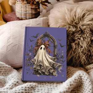 May include: A hardcover journal with a purple cover featuring a central illustration of a ghost draped in lace, wearing a large patterned bow, positioned in front of an arched window frame surrounded by small flying bats and dark foliage.