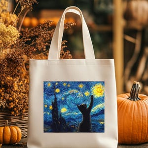 May include: Cream-colored tote bag featuring a vibrant print of Van Gogh's "Starry Night" with a black cat reaching for the stars. The bag has sturdy handles and is surrounded by autumn-themed decorations, including pumpkins and dried foliage.