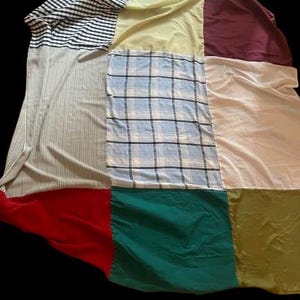 Könnte beinhalten: Eine Patchwork-Decke aus verschiedenen Stoffen in verschiedenen Farben und Mustern, darunter Streifen, Karos und einfarbige Stoffe. Die Decke besteht aus neun Quadraten, jedes mit einem anderen Stoff.