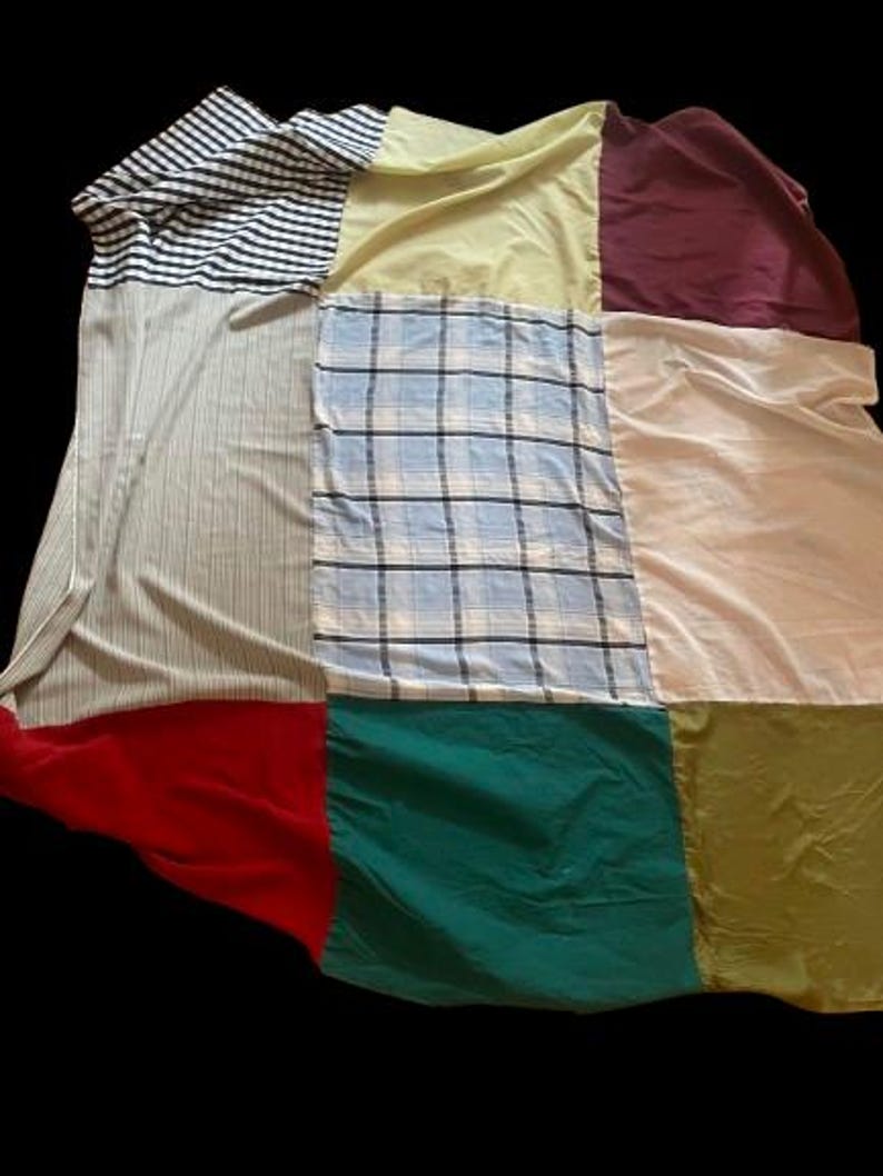 Op de afbeelding: Een patchworkdeken gemaakt van verschillende stoffen in verschillende kleuren en patronen, waaronder strepen, ruitjes en effen kleuren. De deken bestaat uit negen vierkanten, elk met een andere stof.