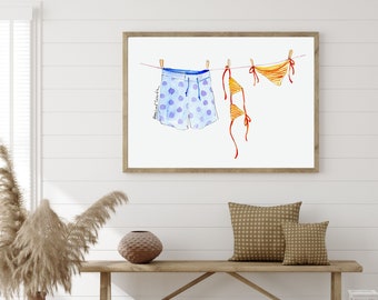 May include: Watercolor painting of a blue and white patterned swimsuit and a yellow and orange bikini hanging on a clothesline. The painting is framed and hanging on a white wall.