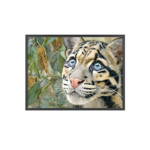 May include: A framed print of a clouded leopard's face, with bright blue eyes and a pink nose. The leopard's coat has black markings on a tan background. Green and brown leaves form the backdrop to the animal's portrait.