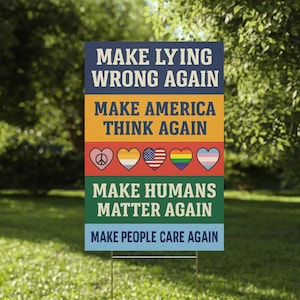 May include: A rectangular yard sign with the phrases "MAKE LYING WRONG AGAIN", "MAKE AMERICA THINK AGAIN", "MAKE HUMANS MATTER AGAIN", and "MAKE PEOPLE CARE AGAIN". The sign has a metal stake and is in a grassy yard.