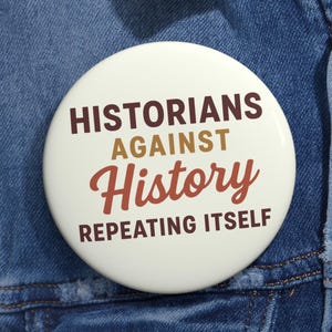Puede incluir: Un botón redondo blanco con el texto "HISTORIANS AGAINST History REPEATING ITSELF" en letras marrones y rojas. El botón está prendido a una chaqueta vaquera azul.
