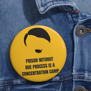 May include: A yellow badge featuring a black hair silhouette and a map of the USA. The text on the badge reads: "PRISON WITHOUT DUE PROCESS IS A CONCENTRATION CAMP."